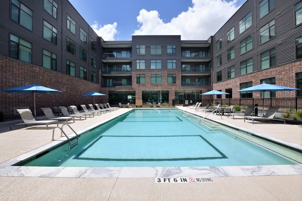 A large swimming pool in front of a building with lounge chairs and umbrellas.