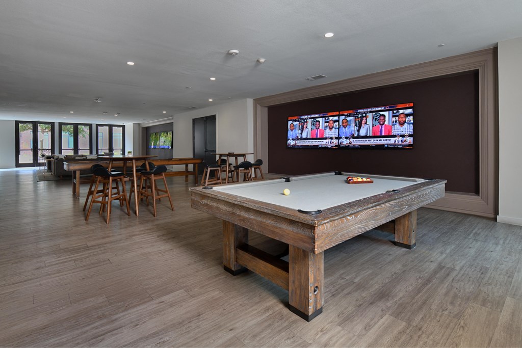 A pool table in a room with wooden floors and a television mounted on the wall.