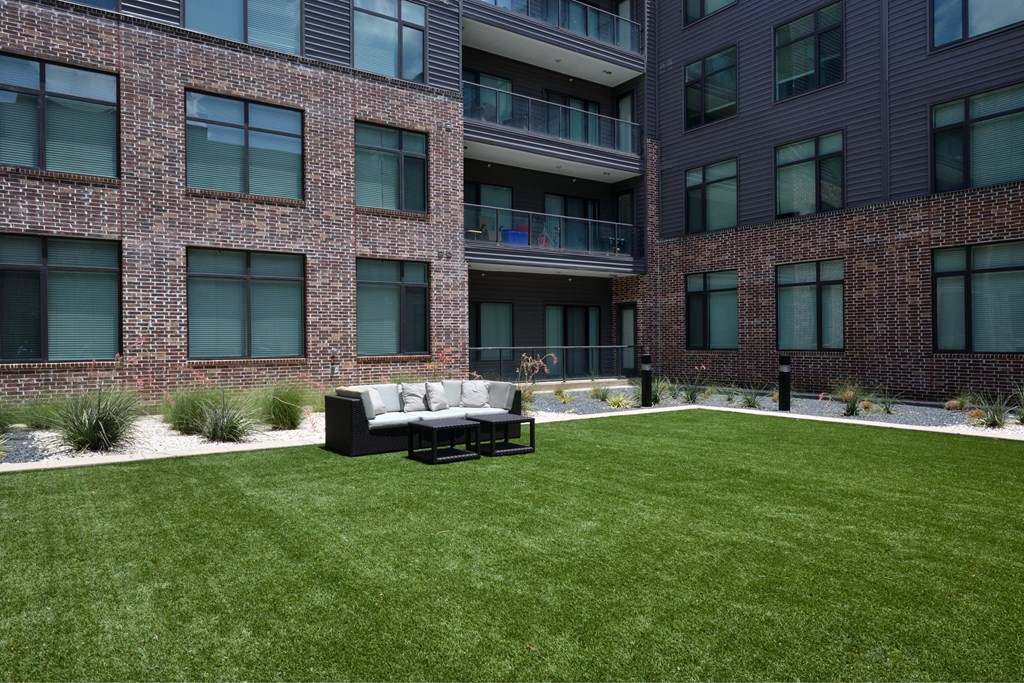 A large lawn in front of a brick building with a white couch and a black coffee table.
