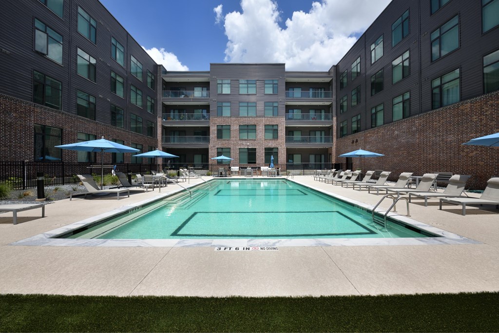 A large swimming pool in front of a building with lounge chairs and umbrellas.