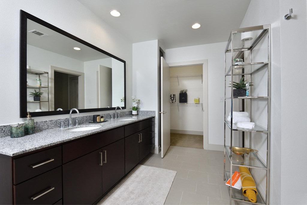 A bathroom with a large mirror, two sinks, and a shelf with towels and plants.
