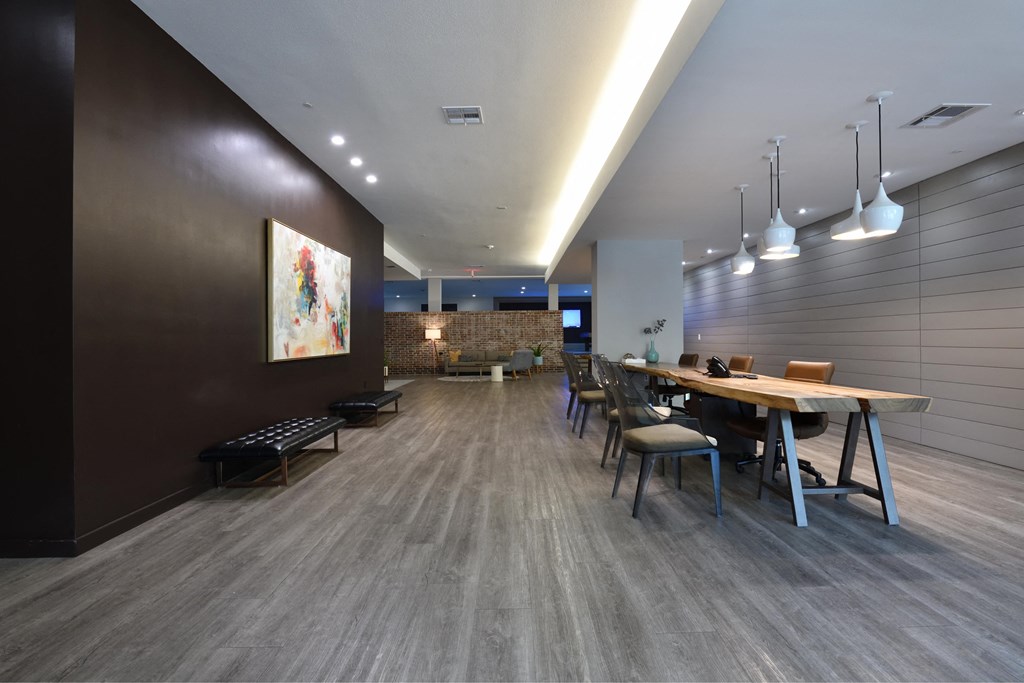 A long wooden table is surrounded by chairs in a room with a brown wall and a painting hanging on it.