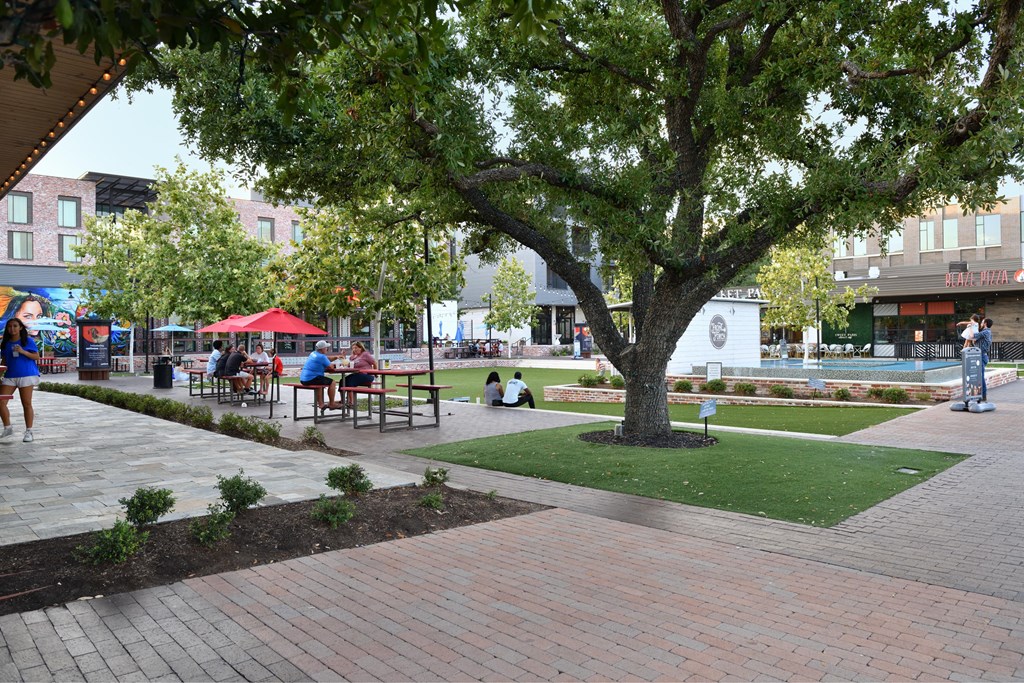 A tree in a park with people sitting at tables under umbrellas.