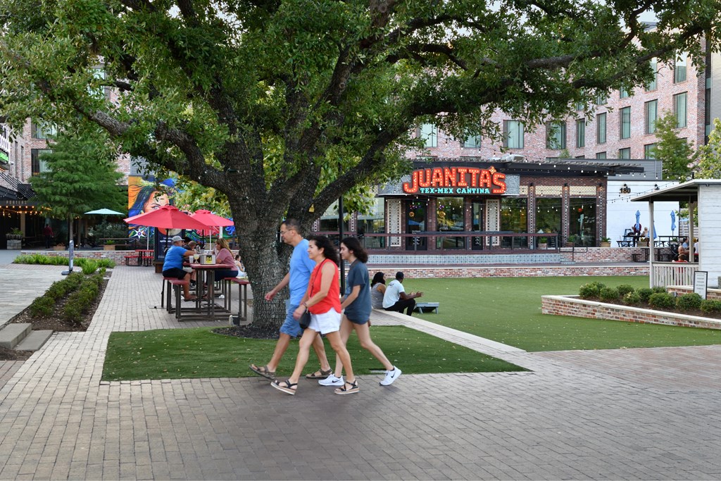 A group of people are walking in front of a tree and a restaurant.