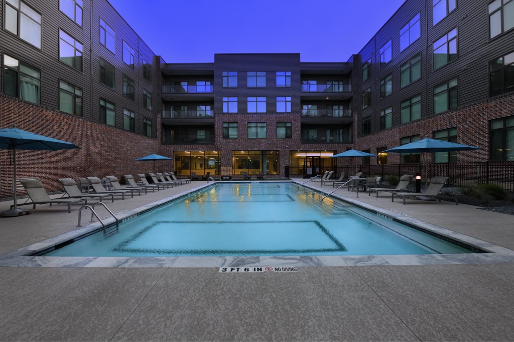 A swimming pool in a courtyard surrounded by chairs and umbrellas.