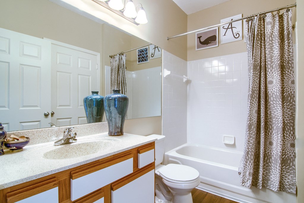 Enclave at Wolfchase Apartments in Cordova Tennessee photo of a bathroom with a white toilet next to a bathtub with a shower curtain