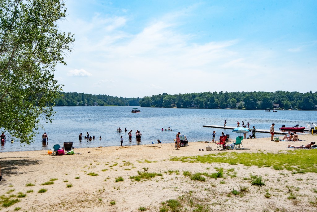 Crowded beach scene with people swimming, sunbathing, and playing in the sand on a sunny day.