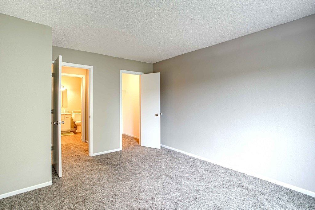 an empty bedroom with open doors to a bathroom