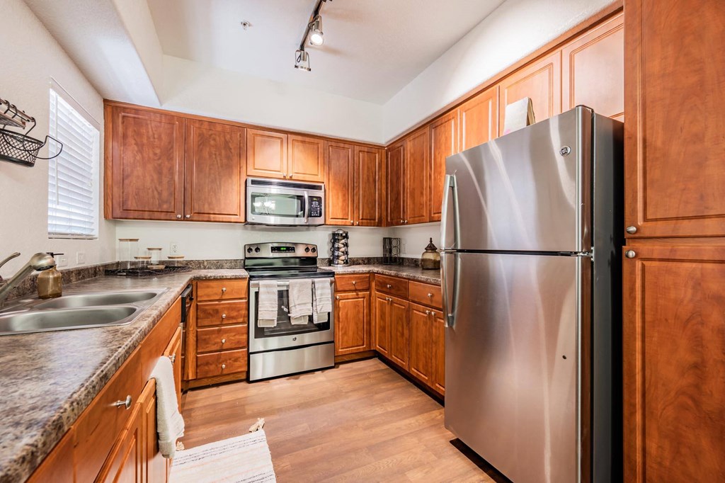 Two-Bedroom Apartments in West Phoenix, AZ - Del Mar - Large Gourmet Kitchen with Wood-Style Cabinets, Hardwood Flooring, Granite Counters, a Window, and Stainless Steel Appliances