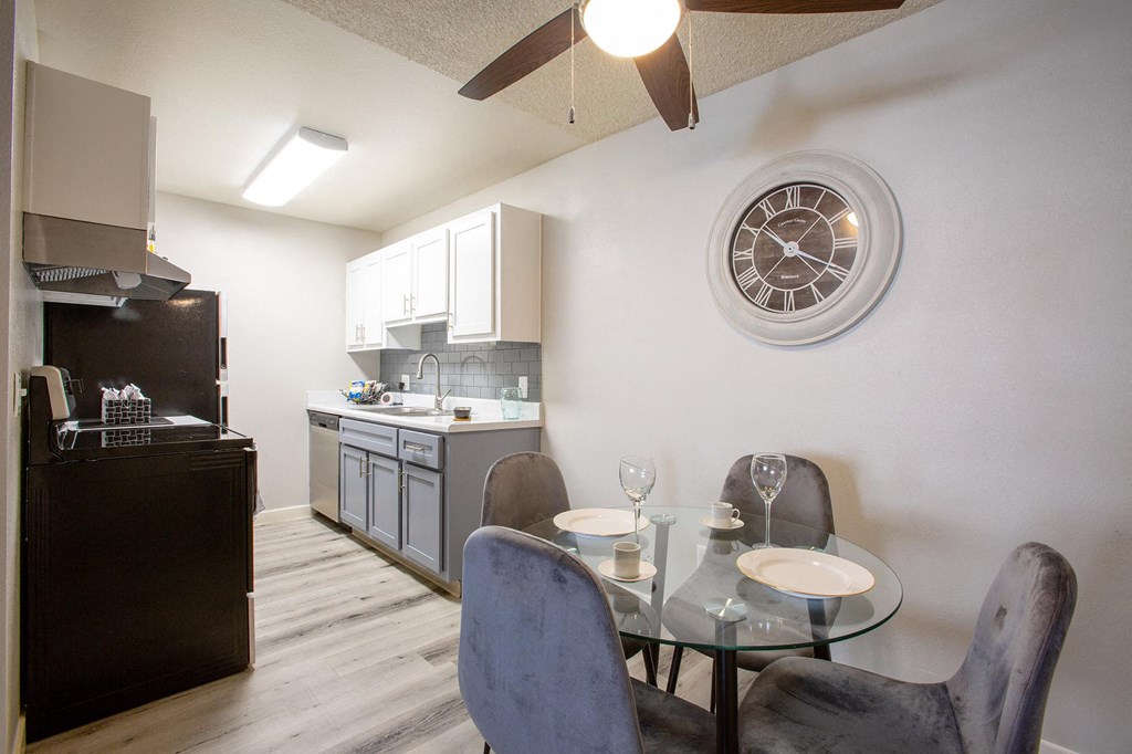 a dining room table with chairs and a kitchen with a clock on the wall