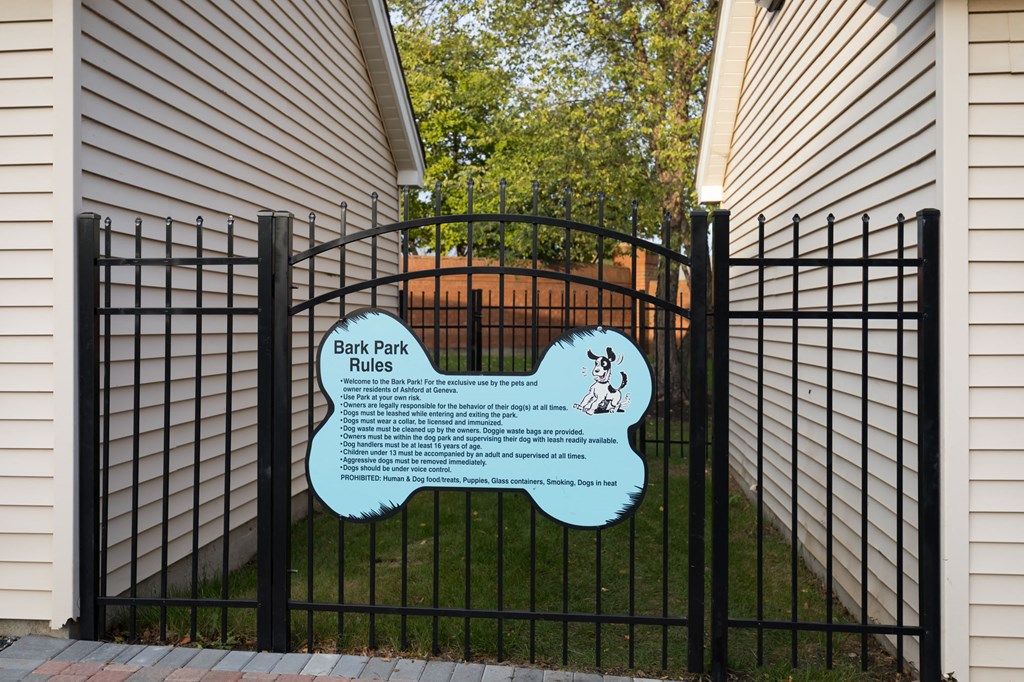 a sign on a fence in front of a house saying dog park rules