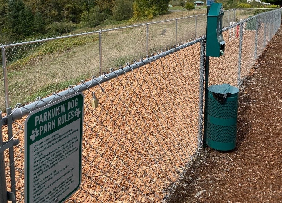 a park rules sign next to a chain link fence and a trash can