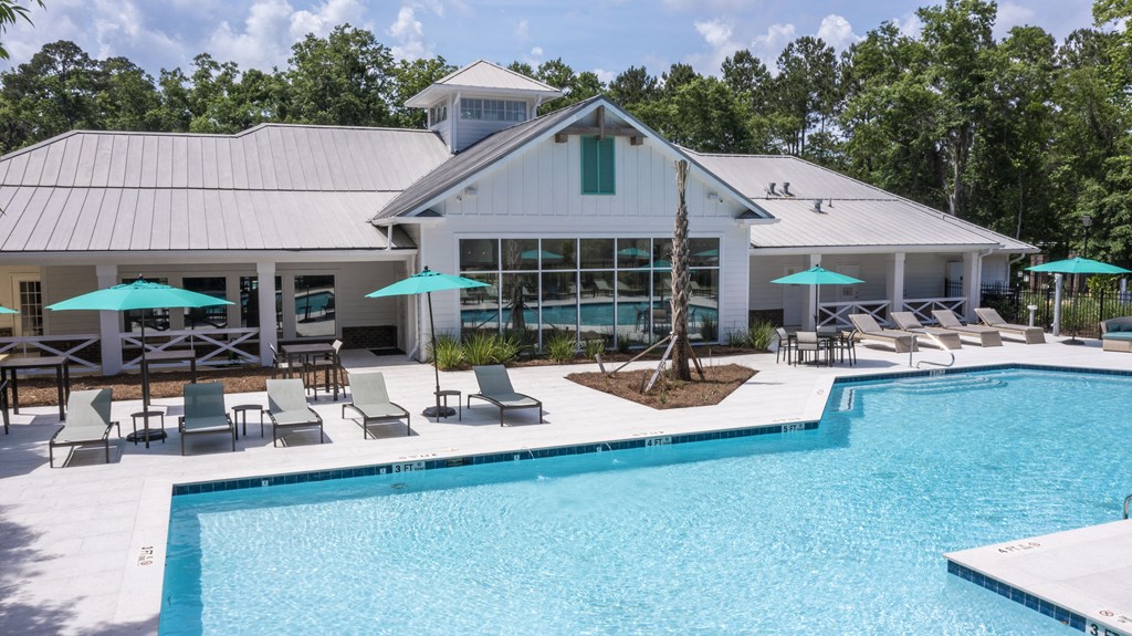 a swimming pool with chaise lounge chairs and umbrellas in front of a white building