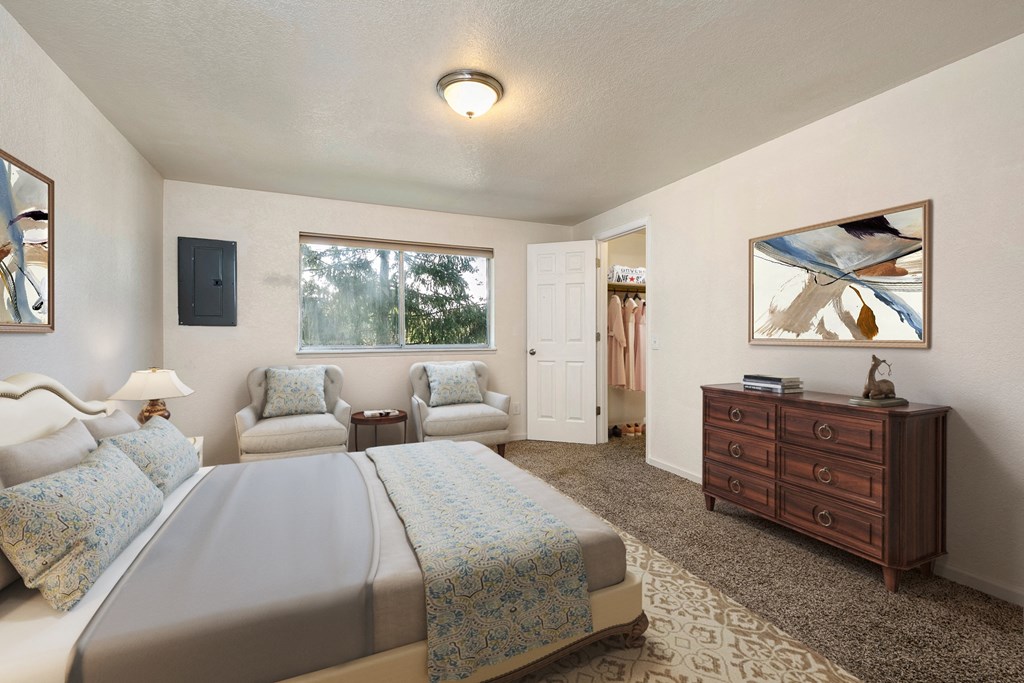 Apartments for Rent in Lynnwood, WA - Evergreen Grove - Bedroom with Carpet Flooring, Full-Size Bed, Nightstand with Lamp, Armchairs, Round Table, Dresser, Large Window, and Spacious Closet.