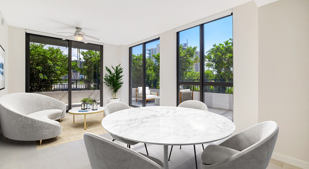 a living room with a round table and chairs and large windows