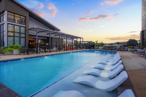 Luxury Apartments in Denver, CO, with In-Unit Washer and Dryer - Edera - Resort Style Pool With In-Water Lounge Chairs, Sundeck Seating, Modern Building Exterior, And Sunset Sky