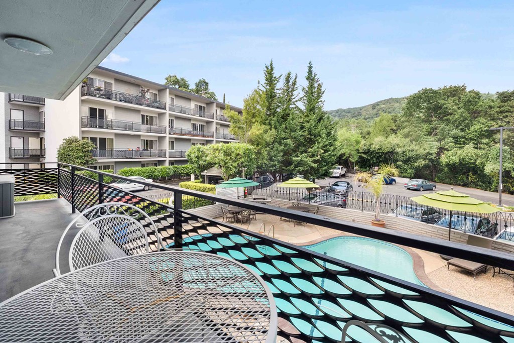 Los Gatos, CA, Apartments - El Gato Penthouse - Balcony with View of Pool Area, Parking Lot, Trees, and Adjacent Apartment Building.
