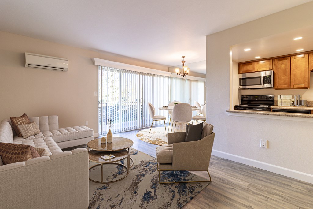Apartments in Los Gatos, CA, for Rent - El Gato Penthouse - Furished Living Room with Wood-Style Flooring, Area Rug, White Sectional Couch, Beige Armchair, Coffee Table, and View of Kitchen and Dining Area with Sliding Glass Doors.