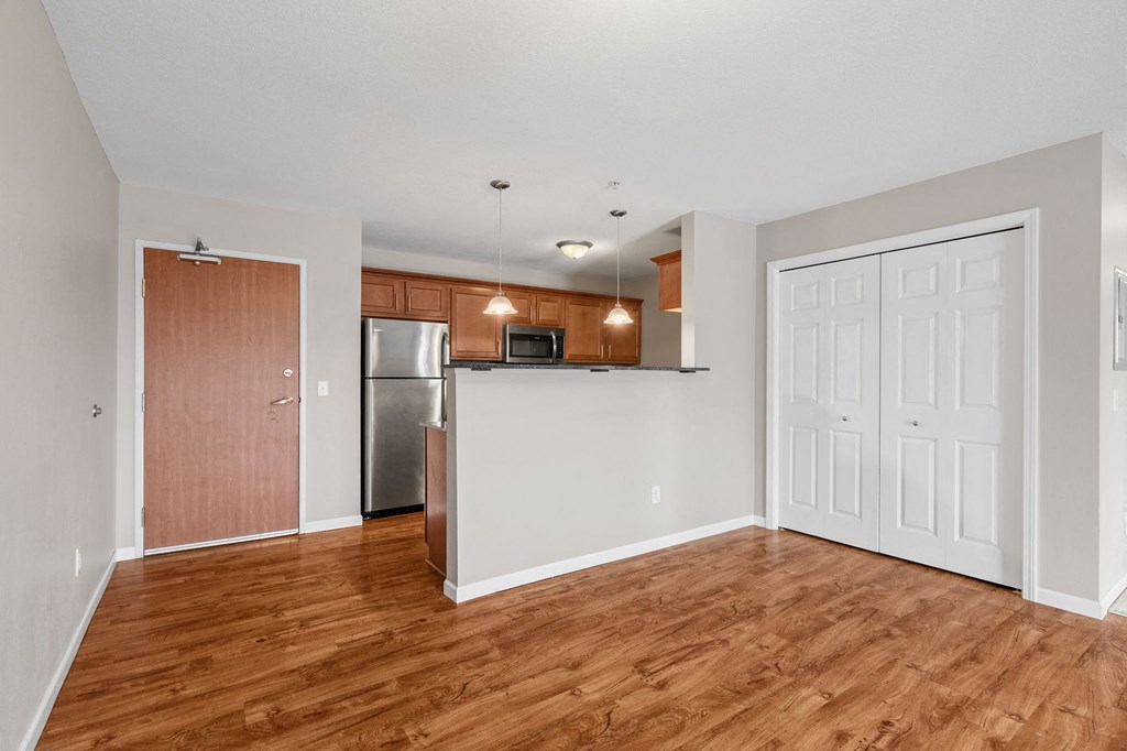 an empty living room with wood flooring and a kitchen with stainless steel appliances