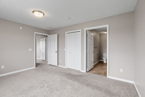 a bedroom with a carpeted floor and doors to a bathroom and a closet