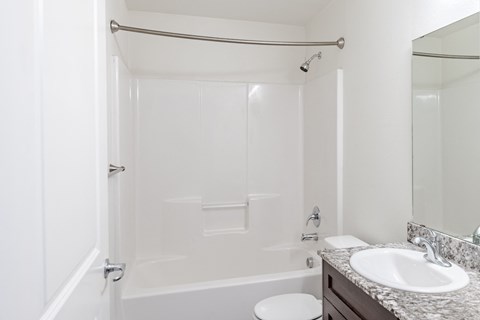 A white bathroom with a toilet, sink, and bathtub A kitchen with a granite countertop and stainless steel appliances at Emerald Crest, Washington, 98011
