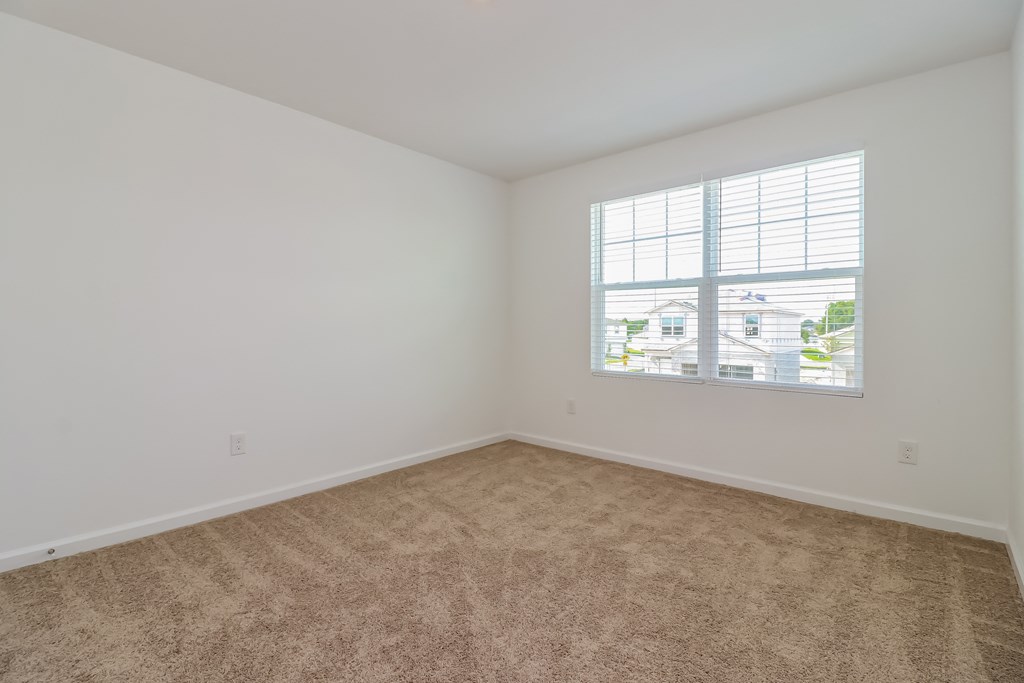 A room with a carpeted floor and a window showing a view of houses.