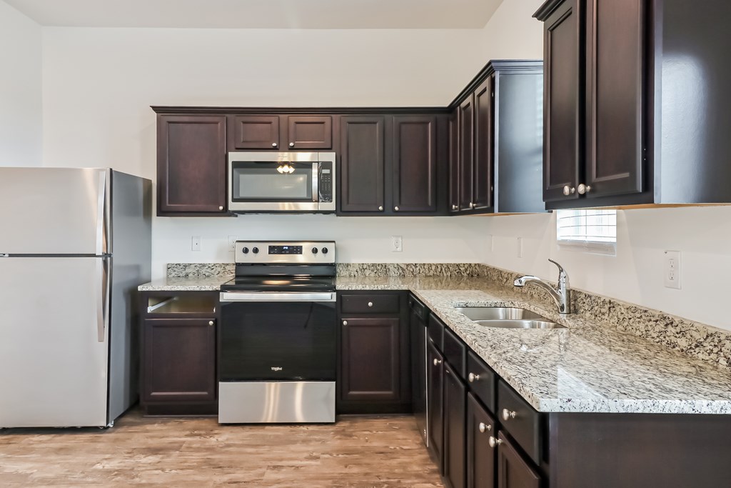 A kitchen with dark brown cabinets and a granite countertop.