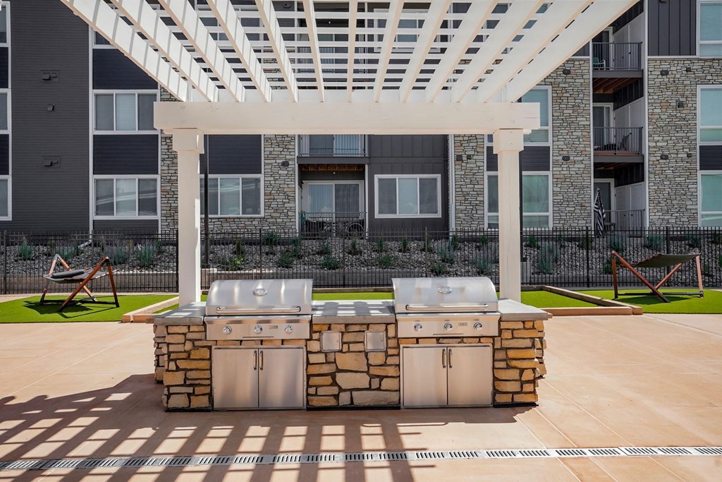 two stainless steel barbecue grills under a white pergola at an apartment building
