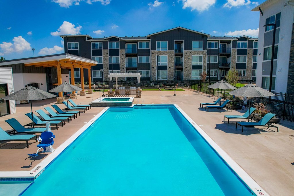 a swimming pool with chairs and umbrellas in front of an apartment building