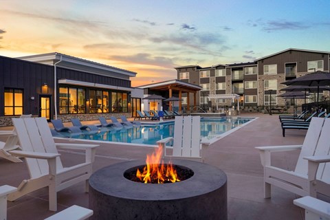 Reunion, CO, Luxury Apartments Near DIA - Enova - Outdoor Pool Deck With Round Fire Pit Table, Adirondack Chairs, Lounge Seating, and Umbrellas.