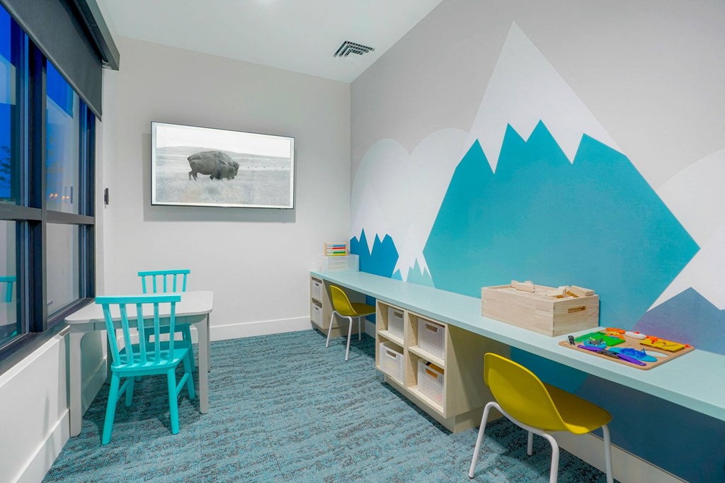 a room with a desk and chairs and a table with a bear on the wall