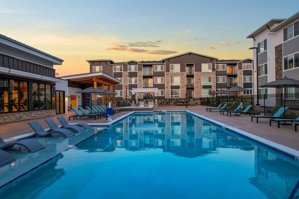 a swimming pool with lounge chairs around it in front of an apartment building