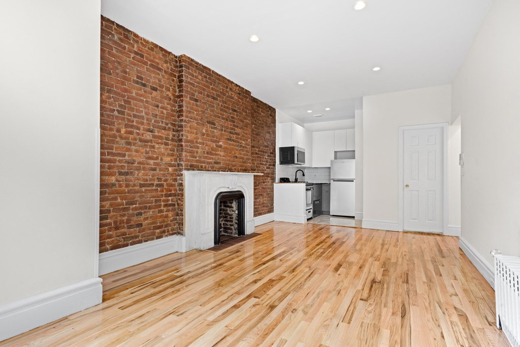 an empty living room with a brick fireplace and wooden floors