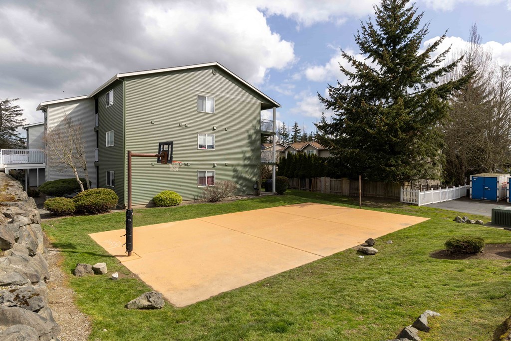 Two-Bedroom Apartments in Lynnwood, WA - Evergreen Grove - Basketball Court with Surrounding Grass, Trees, and View of Building.