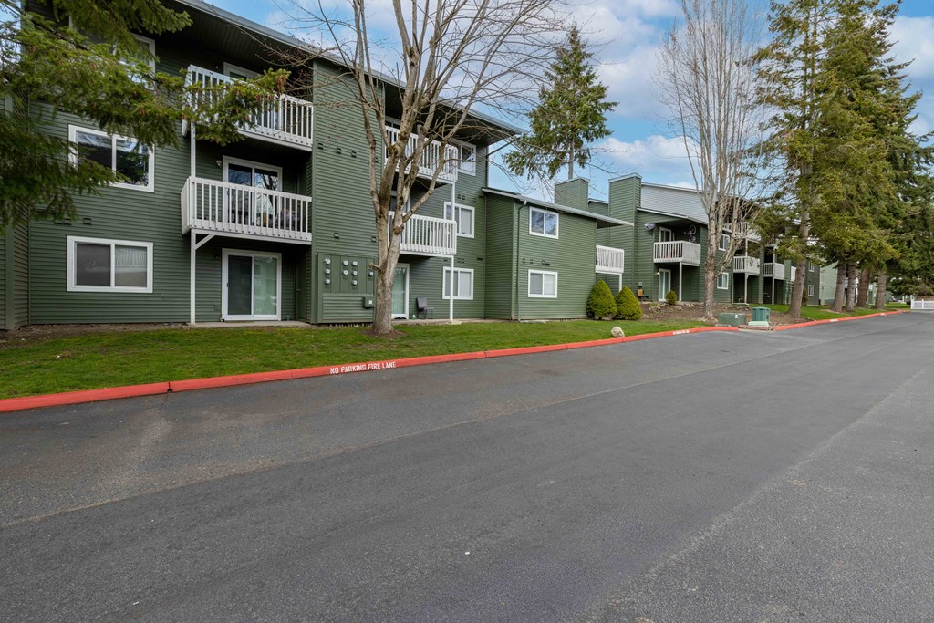 Apartments For Rent In Lynnwood - Evergreen Grove Apartments - Building Exterior With Parking Lot Access, Private Patios, And Tall Trees