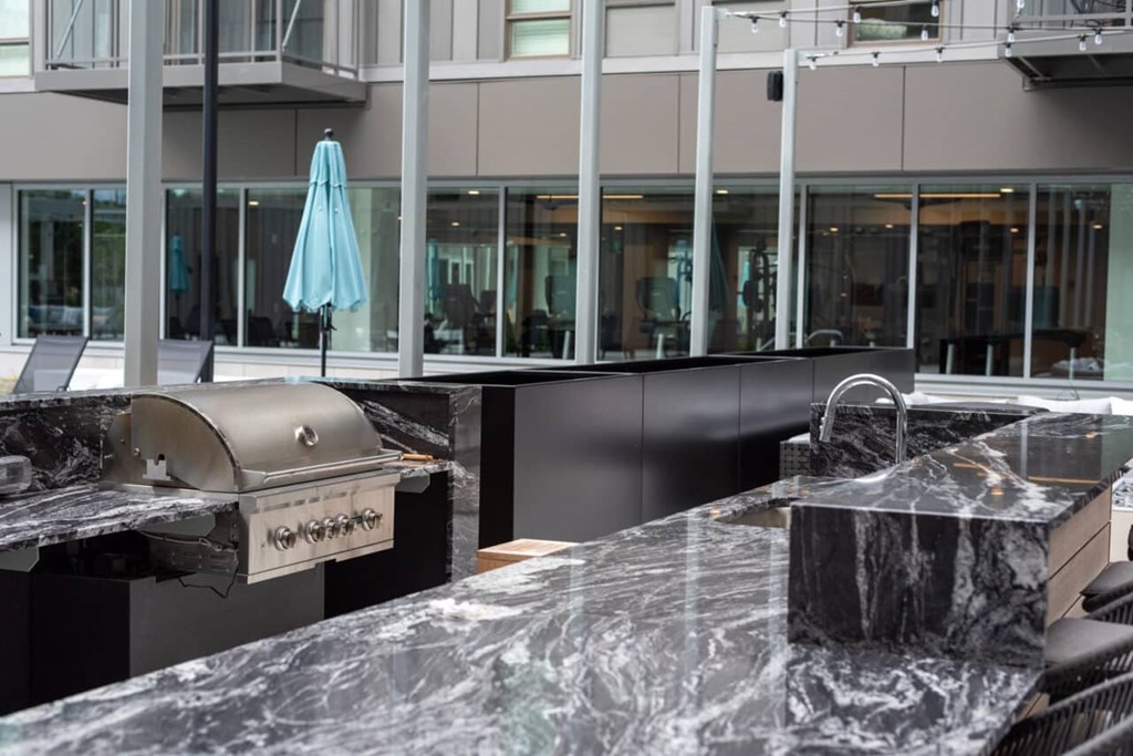 A marble countertop with a grill and umbrella in the background.