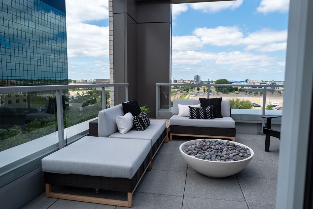 A balcony with two grey cushioned seats and a bowl of stones in the middle.
