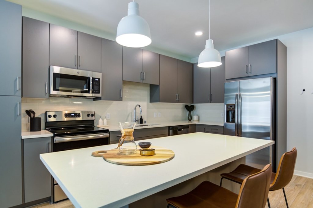 Pet-Friendly Luxury Apartments in Bloomington, MN - The Fenley - A Kitchen with Stainless Steel Appliances, Kitchen Island with Hanging Lights Above, and Brown Chairs