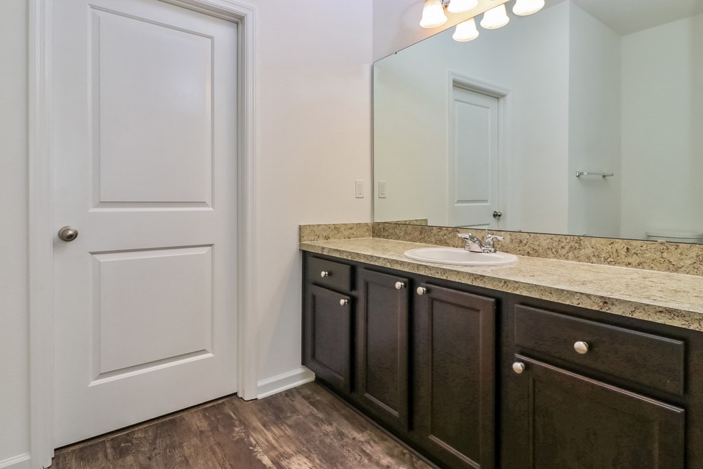 A bathroom with a white door, brown cabinets, and a marble countertop.