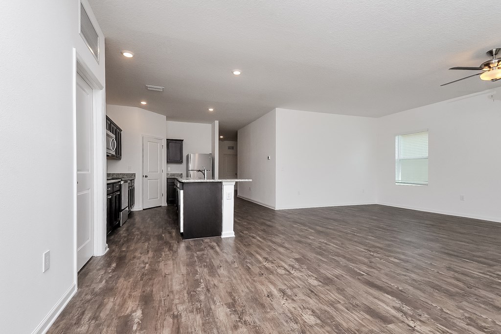 A spacious living room with a kitchen in the background.