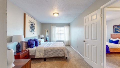 Bedroom at Broad on the Green in Augusta, GA, featuring carpet flooring, a large window, and bright natural light in a pet-friendly apartment community.