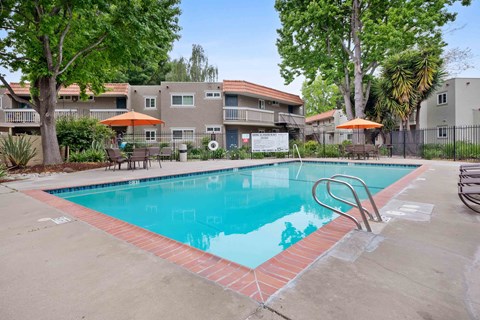 Apartments in Hayward, CA - Glen Oaks Apartments - Swimming Pool With Brick Coping, Patio Seating With Orange Umbrellas, and Mature Trees Surrounding The Community.