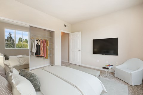 a bedroom with a white bed and a tv on the wall