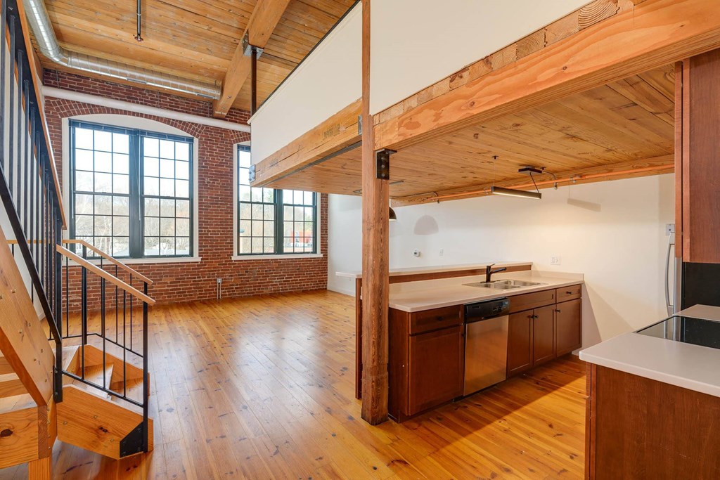 Loft apartment interior with exposed brick, wood beams, stairs, and kitchen.