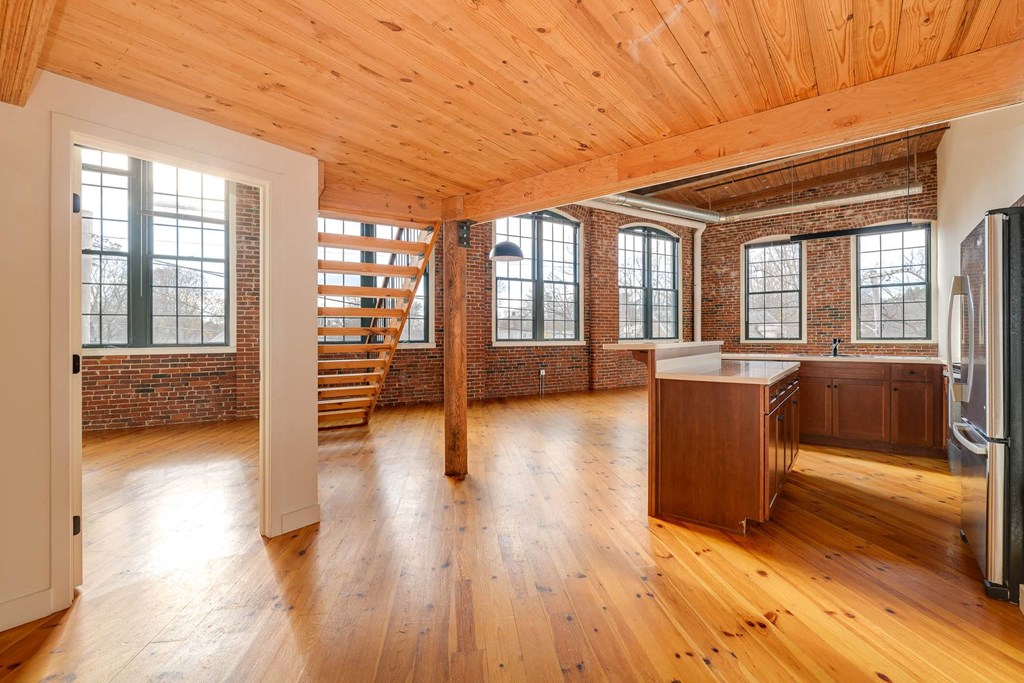 Loft apartment interior with exposed brick walls, wood floors, timber ceiling, and staircase.