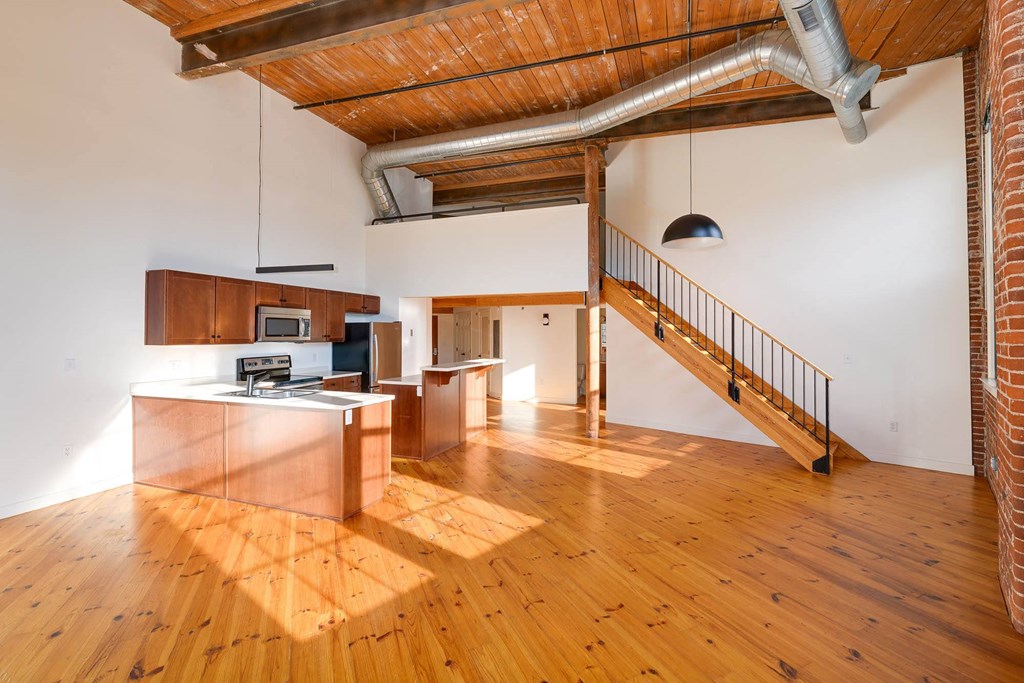 Open-concept loft apartment with kitchen, wooden floors, exposed ductwork, and staircase to upper level.