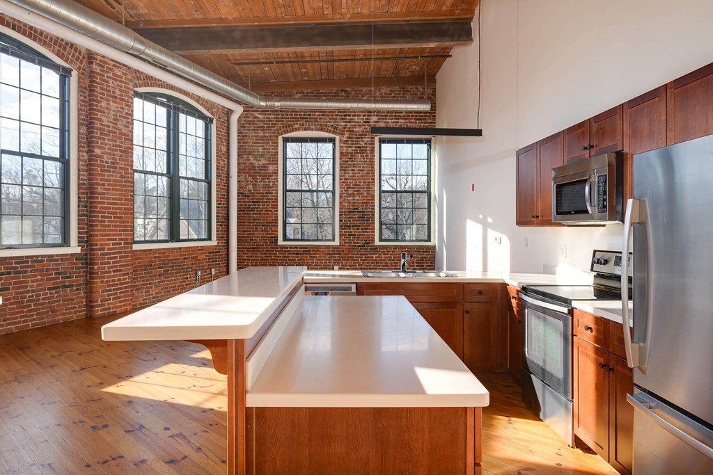Loft apartment kitchen with exposed brick, wood floors, stainless steel appliances, and large windows.