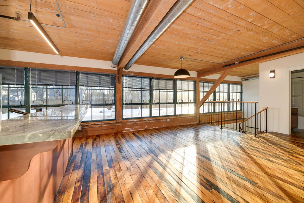 Loft apartment interior with exposed brick, wood beams, stairs, and kitchen.