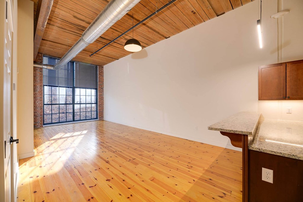 Loft apartment interior with exposed wood ceiling, brick wall, large windows, and kitchen counter.