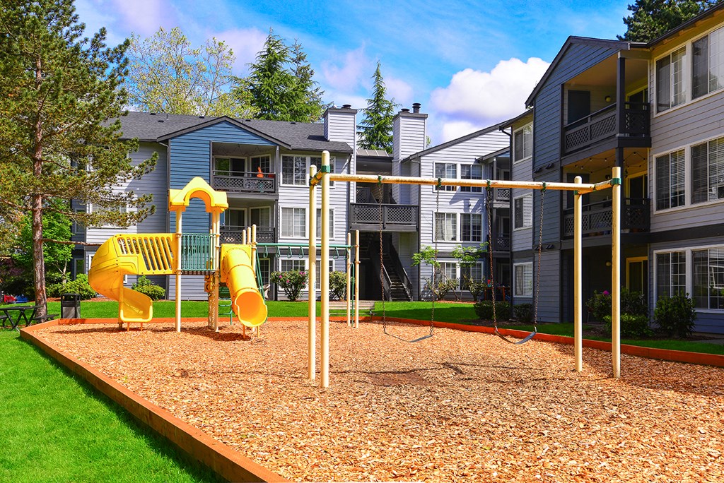 a playground with a yellow swing set in front of apartment buildings